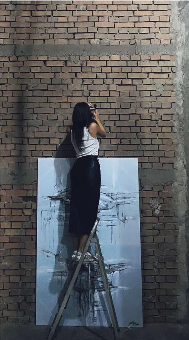Umetnica na merdevinama radi na slici uz zid od opeke